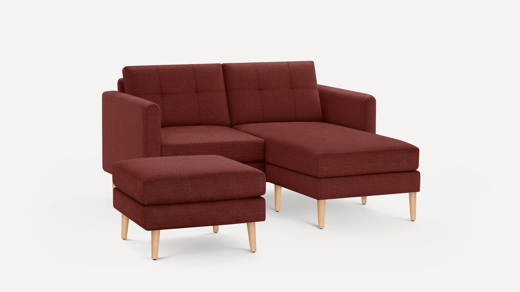 Modern burgundy fabric sectional sofa with tufted back cushions and wooden legs, accompanied by a matching ottoman.