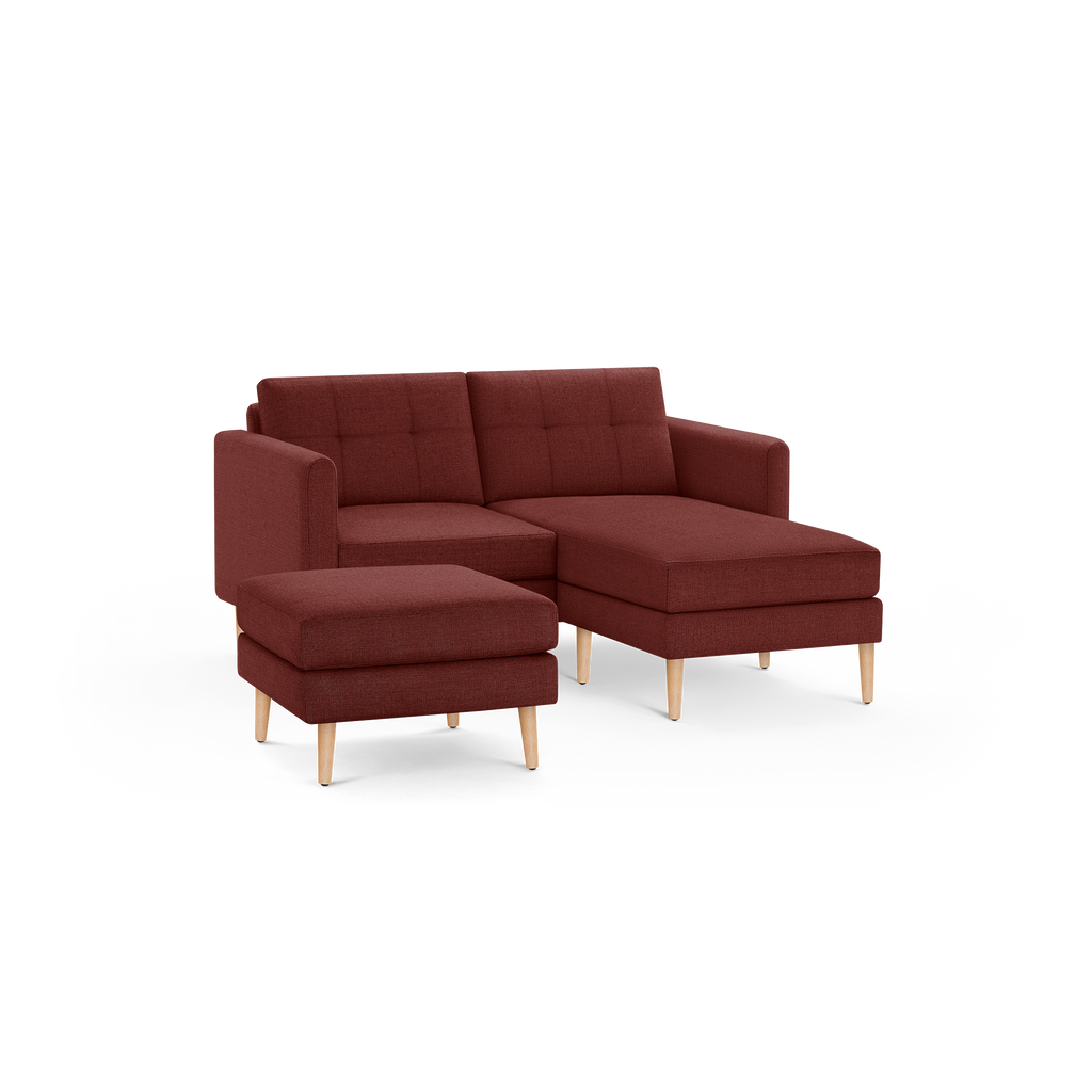 Compact modern sectional sofa in deep red fabric with tufted back cushions and light wooden legs, accompanied by a matching ottoman.