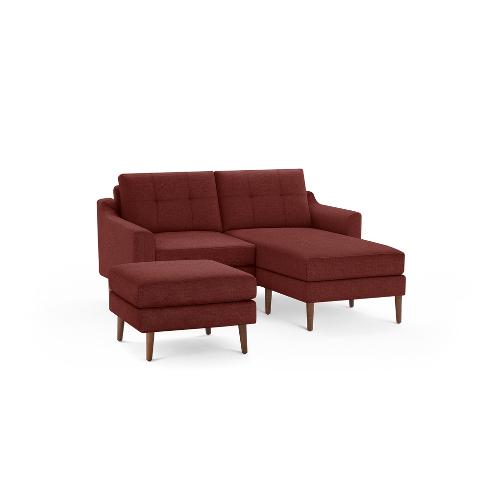 Rust-colored modern sectional sofa with tufted back cushions, matching ottoman, and wooden legs on a black background.
