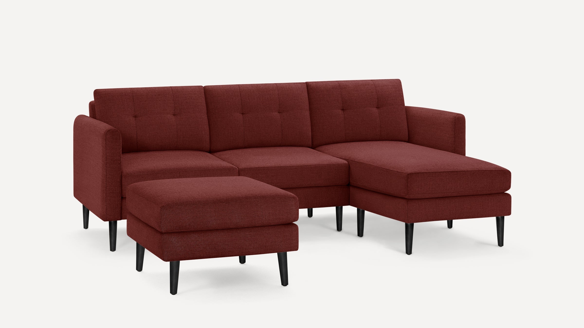 Modern deep red fabric sectional sofa with tufted back cushions and matching ottoman, featuring black tapered legs and clean lines.