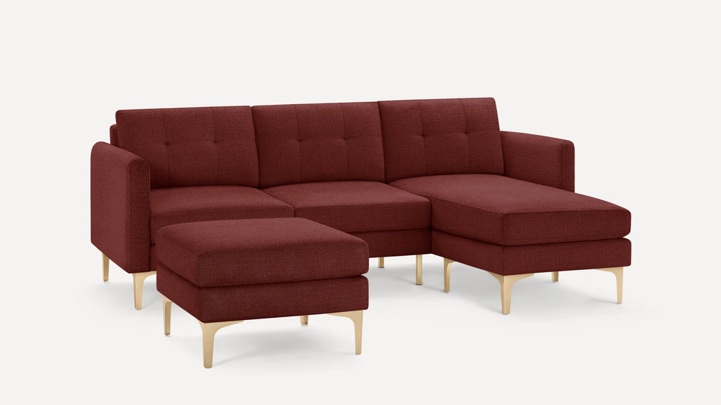 Modern L-shaped sectional sofa in deep red fabric with tufted back cushions and light wooden tapered legs, accompanied by a matching ottoman.
