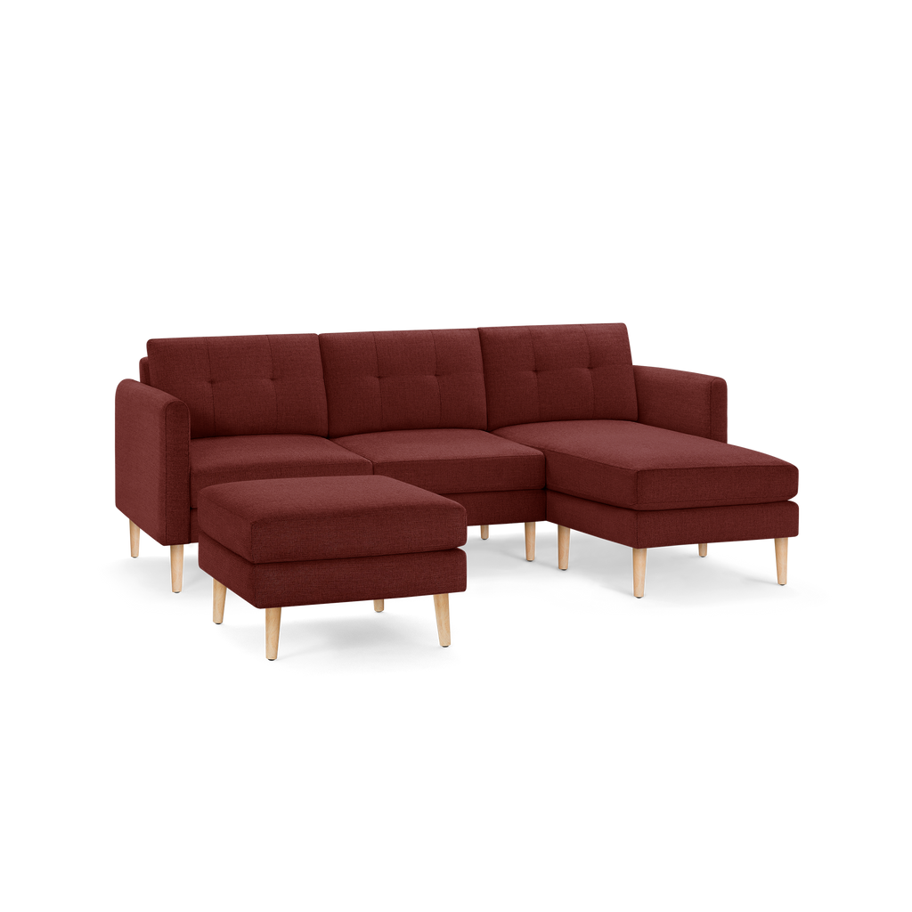 Modern L-shaped sectional sofa in deep red fabric with tufted back cushions and light wooden legs, featuring a matching ottoman.