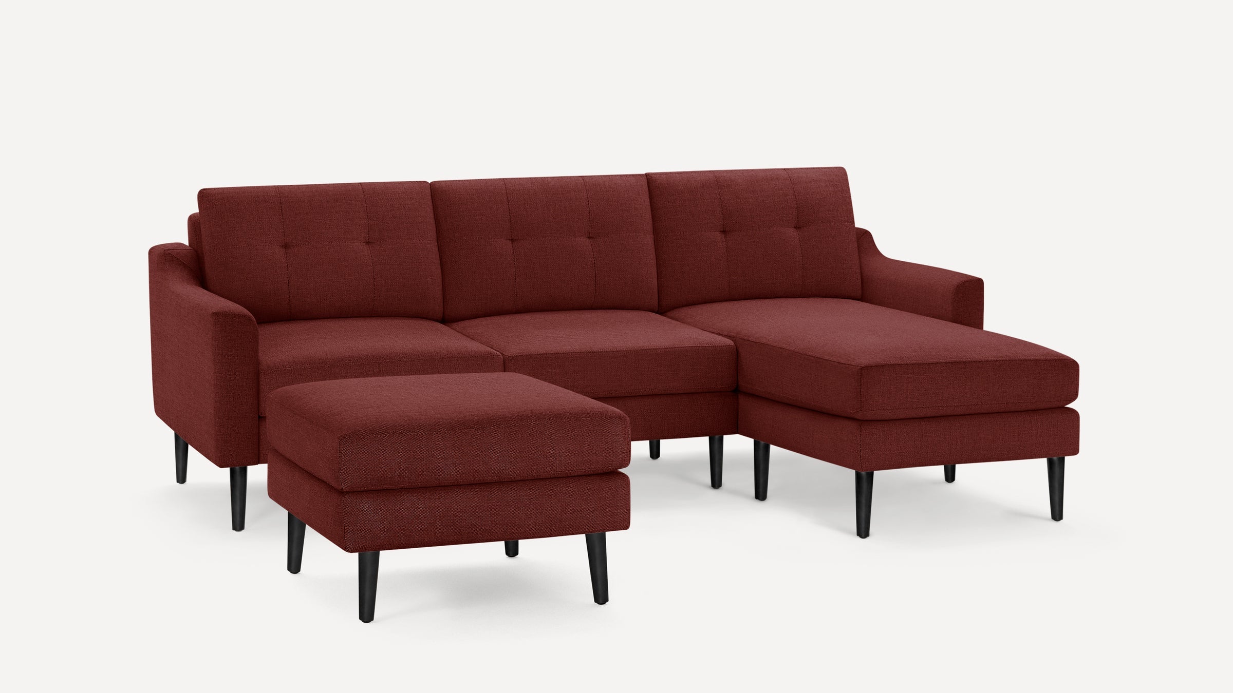 Mid-century style sectional sofa in deep red fabric with tufted cushions, black tapered wooden legs, and matching ottoman.