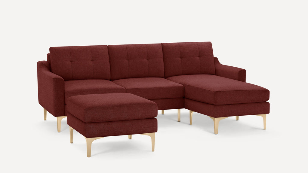 Modern burgundy sectional sofa with tufted cushions, light wooden legs, and a matching ottoman, shown on white background.