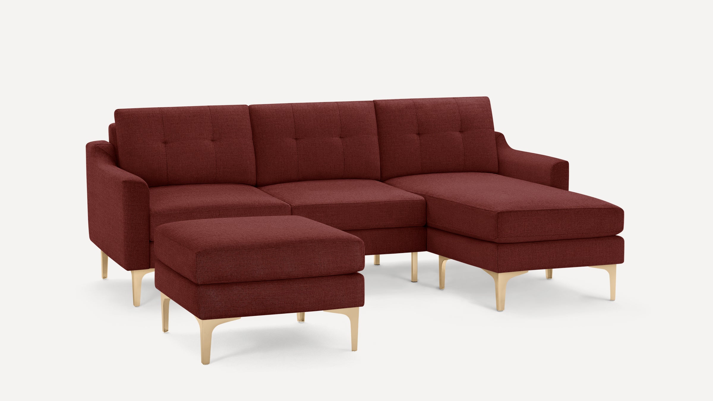 Modern burgundy sectional sofa with tufted cushions, light wooden legs, and a matching ottoman, shown on white background.