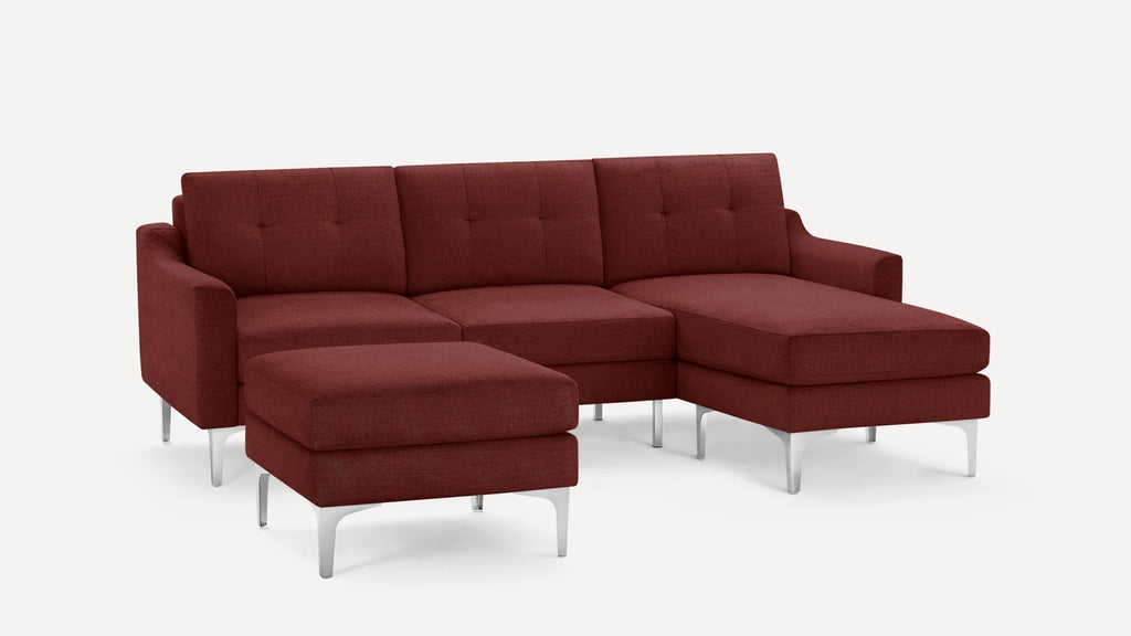 Modern sectional sofa with deep red fabric upholstery, tufted back cushions, metal legs, and matching ottoman on white background.