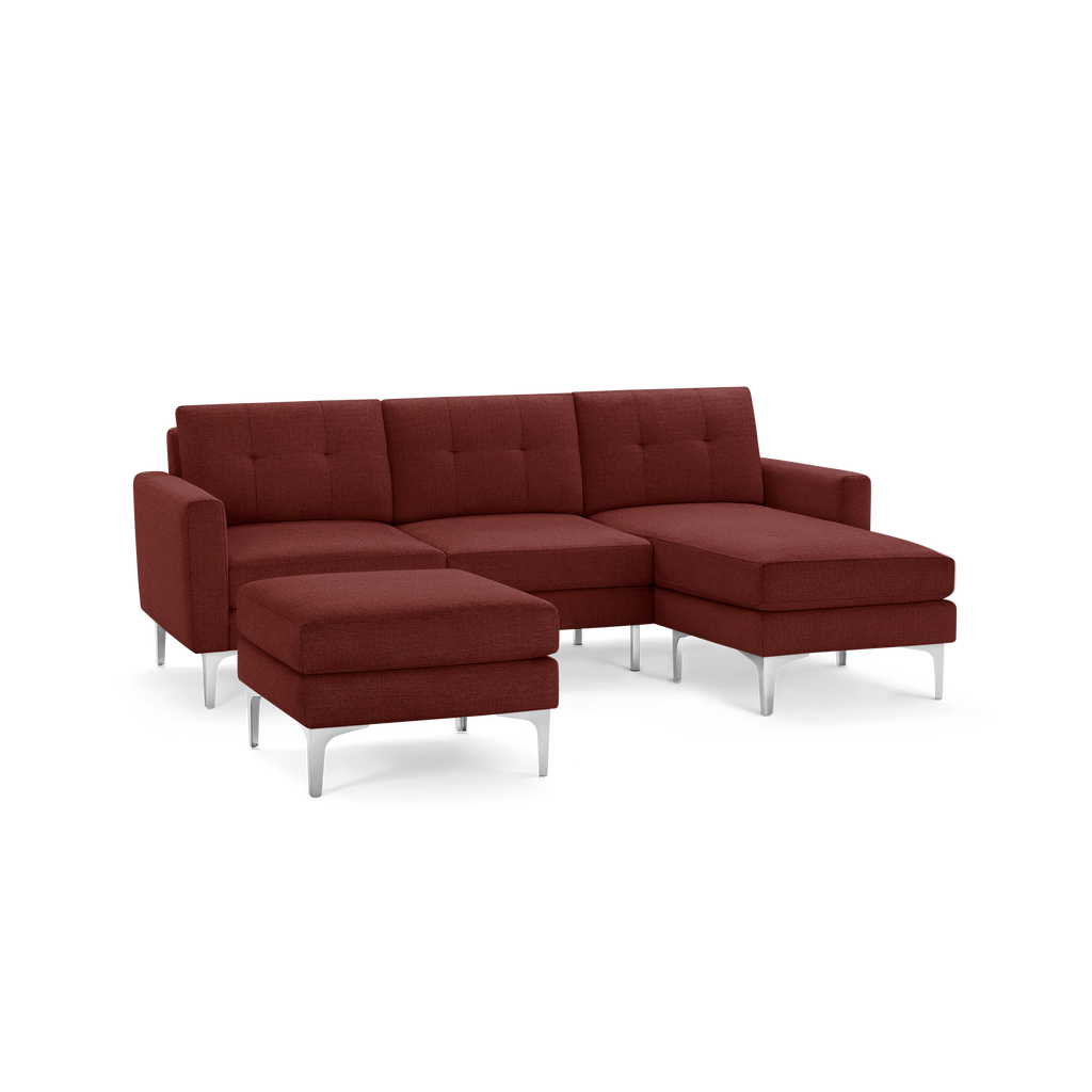Modern sectional sofa in dark red fabric upholstery with tufted back cushions, metal legs, and a matching ottoman.