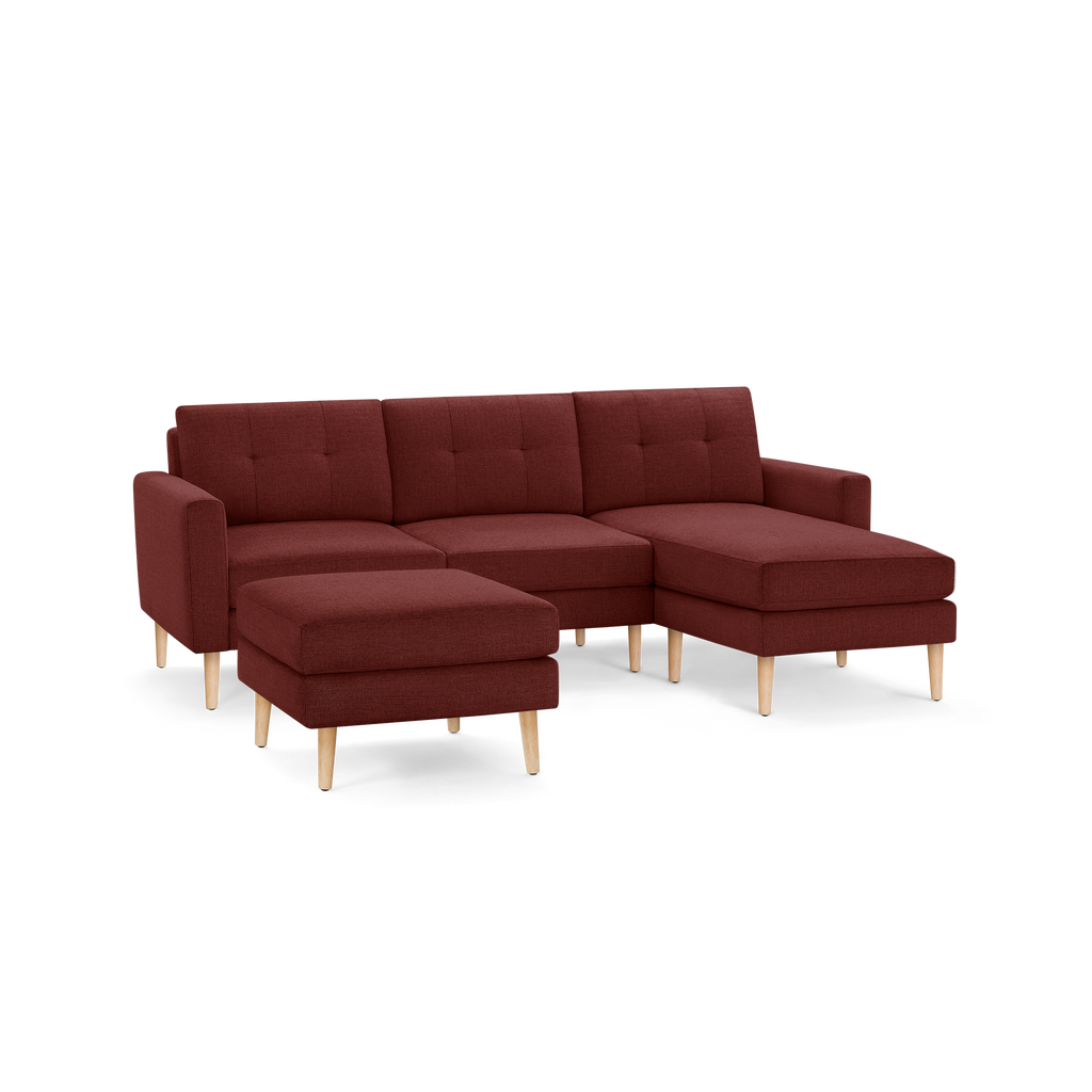 Modern sectional sofa with chaise lounge and matching ottoman, upholstered in deep red fabric with wooden legs.