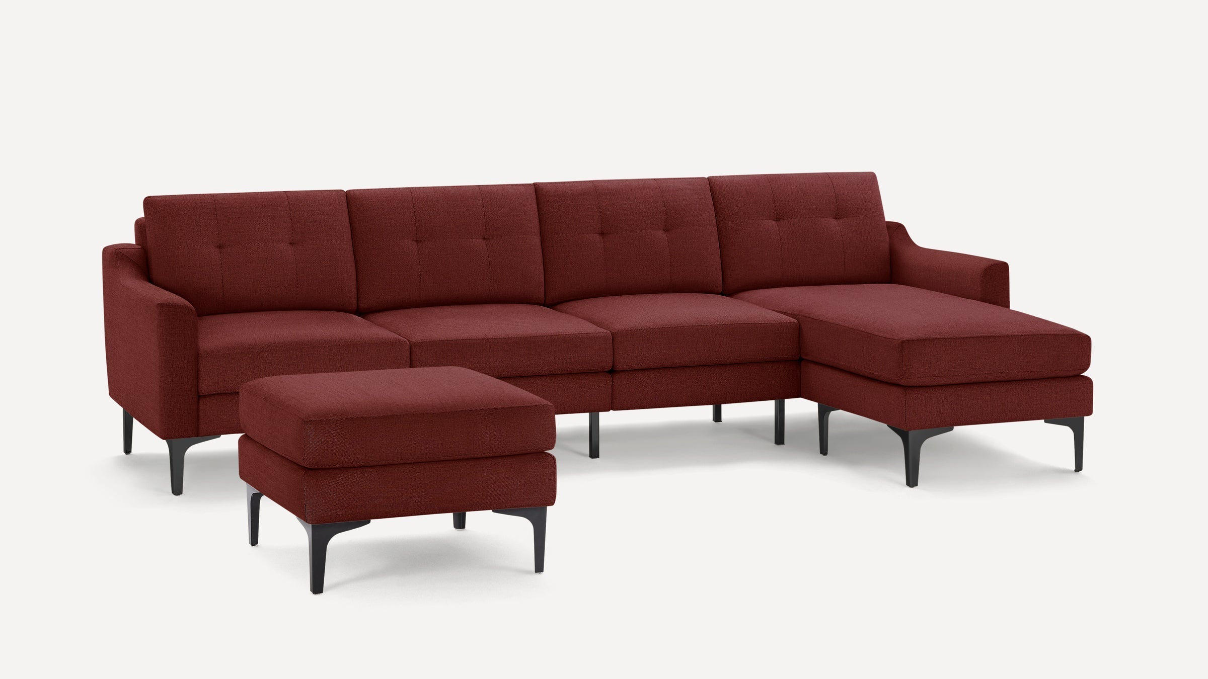 Modern sectional sofa with chaise lounge and matching ottoman in deep burgundy fabric, featuring slim black legs and tufted back cushions.