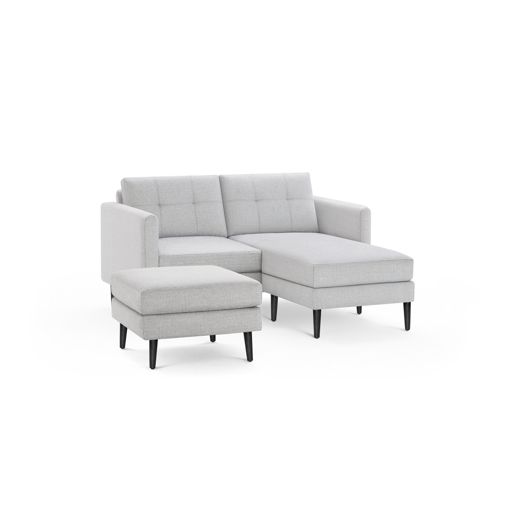 Light gray fabric sectional sofa with tufted back cushions and matching ottoman, featuring black tapered legs.
