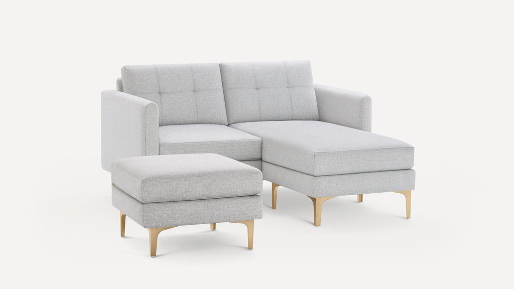 Light gray upholstered modern sectional sofa with tufted back cushions and matching ottoman, featuring gold metal legs.