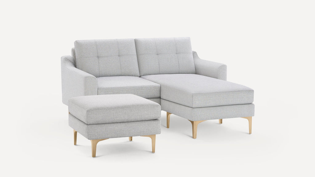 Light gray modern sectional sofa with chaise lounge and matching ottoman, featuring tufted cushions and wooden legs.