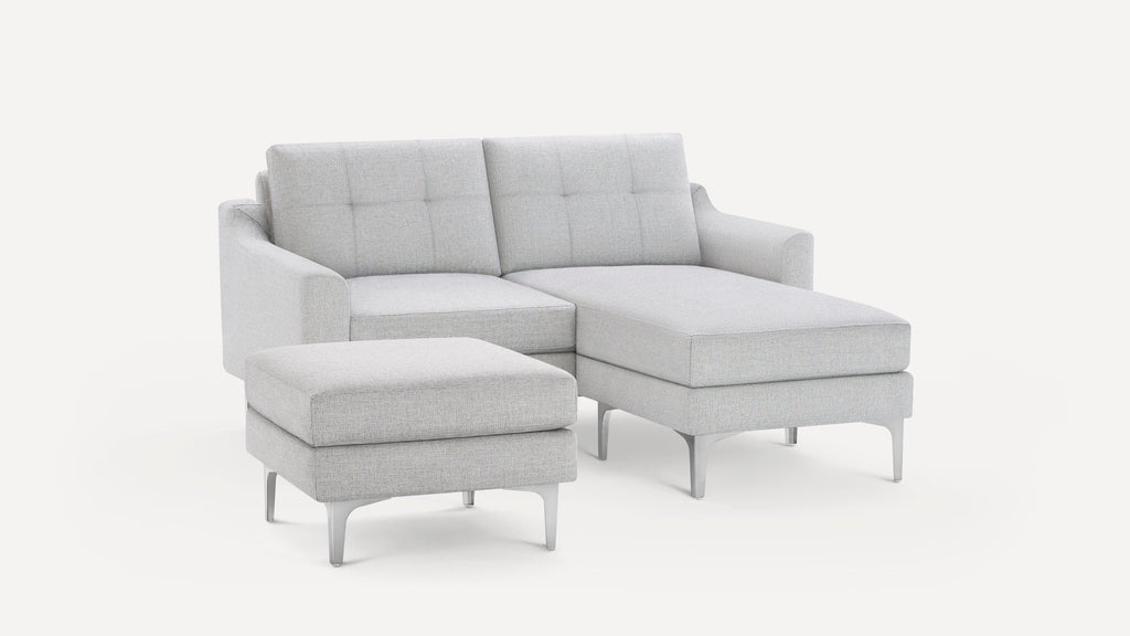 Light gray modern sectional sofa with tufted back cushions and matching ottoman on silver metal legs.