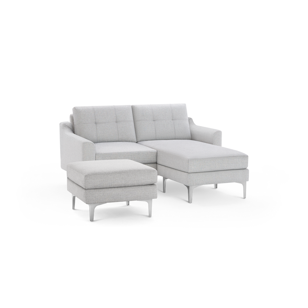 Light gray modern sectional sofa with tufted back cushions and matching ottoman, both supported by slender white legs.