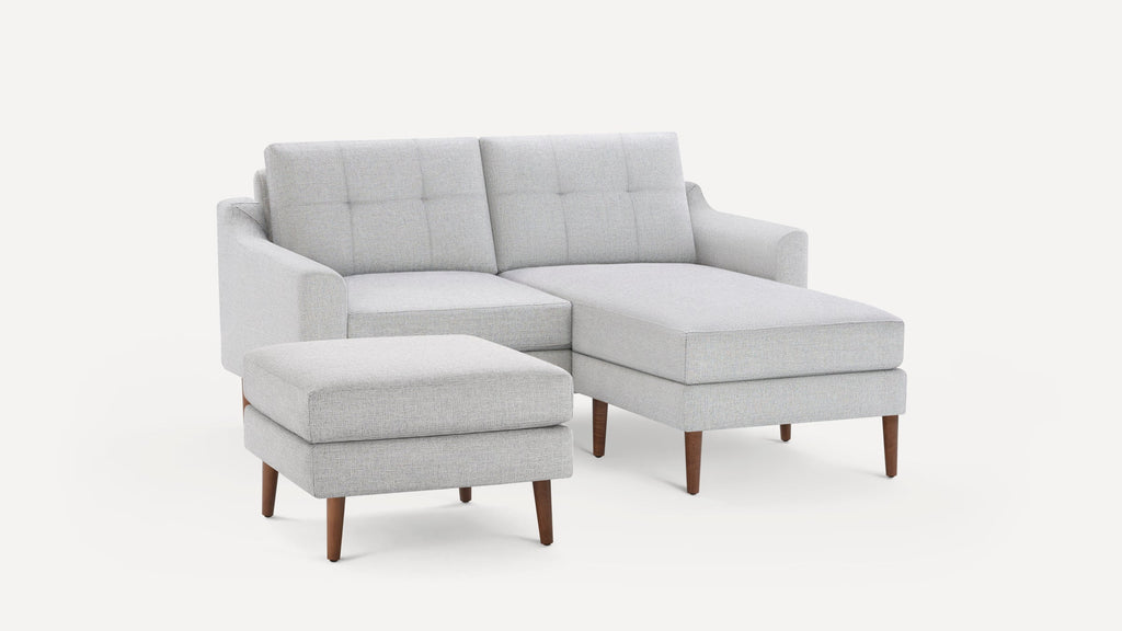 Light gray fabric sectional sofa with tufted back cushions, wooden legs, and a matching ottoman on a white background.