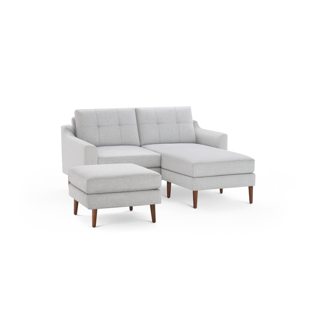 Light gray sectional sofa with tufted back cushions and wooden legs, featuring a chaise and matching ottoman.
