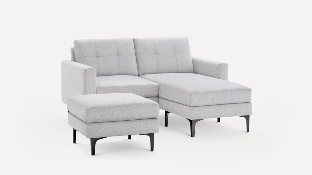 Light gray fabric sectional sofa with chaise lounge and matching ottoman on black metal legs, modern and minimalist design.