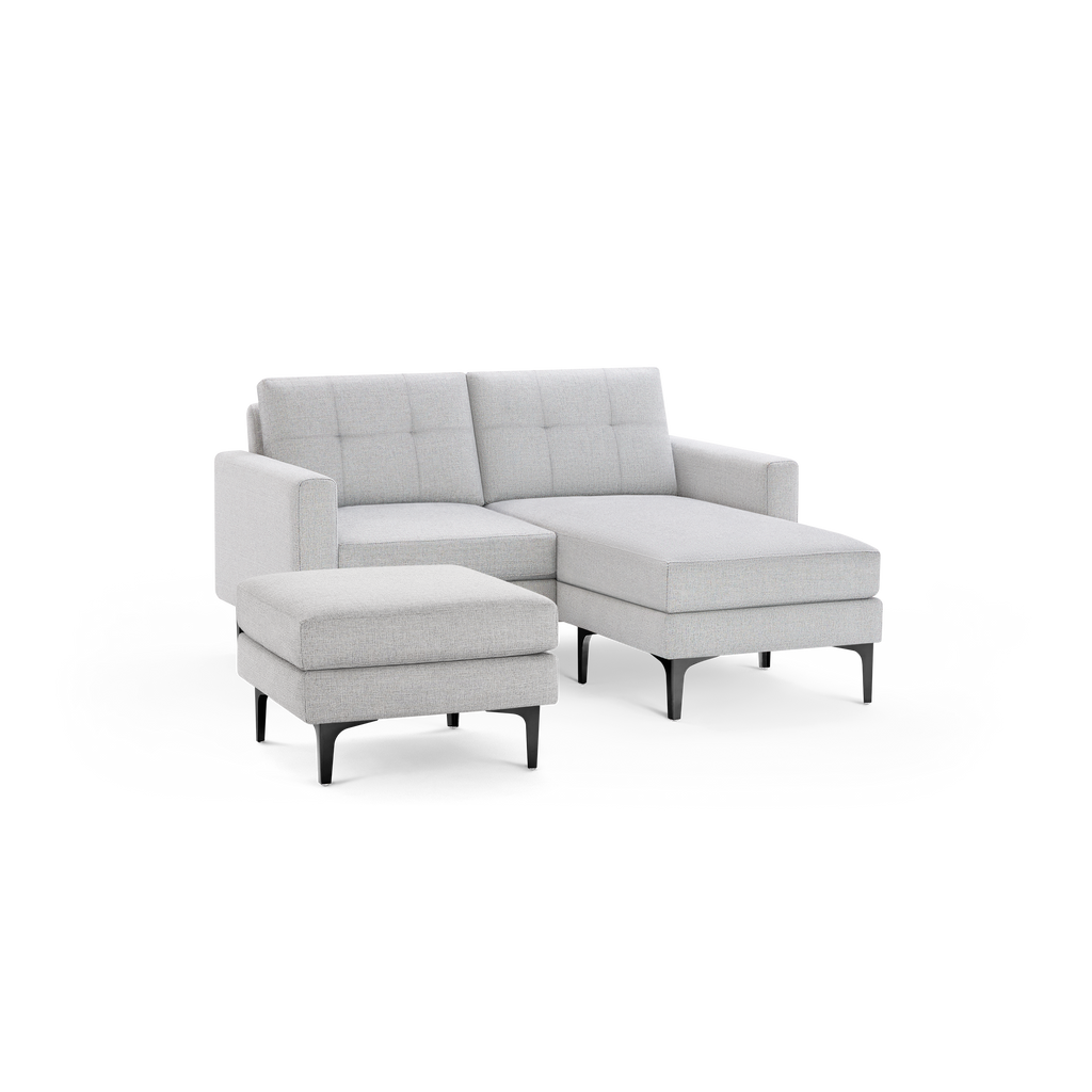 Light gray fabric sectional sofa with tufted back cushions, right chaise lounge, matching ottoman, and sleek black legs.
