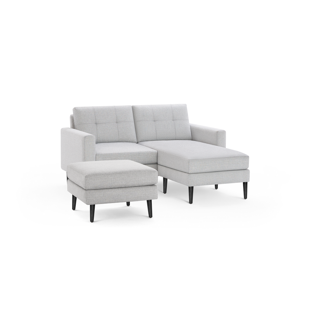 Light gray upholstered sectional sofa with tufted back cushions, wooden legs, and matching ottoman on black background.