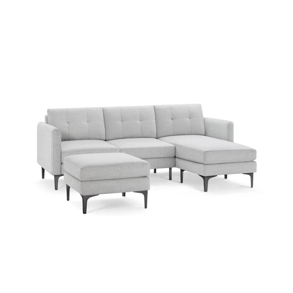 Light grey fabric sectional sofa with tufted back cushions, chaise lounge, and matching ottoman on black legs.