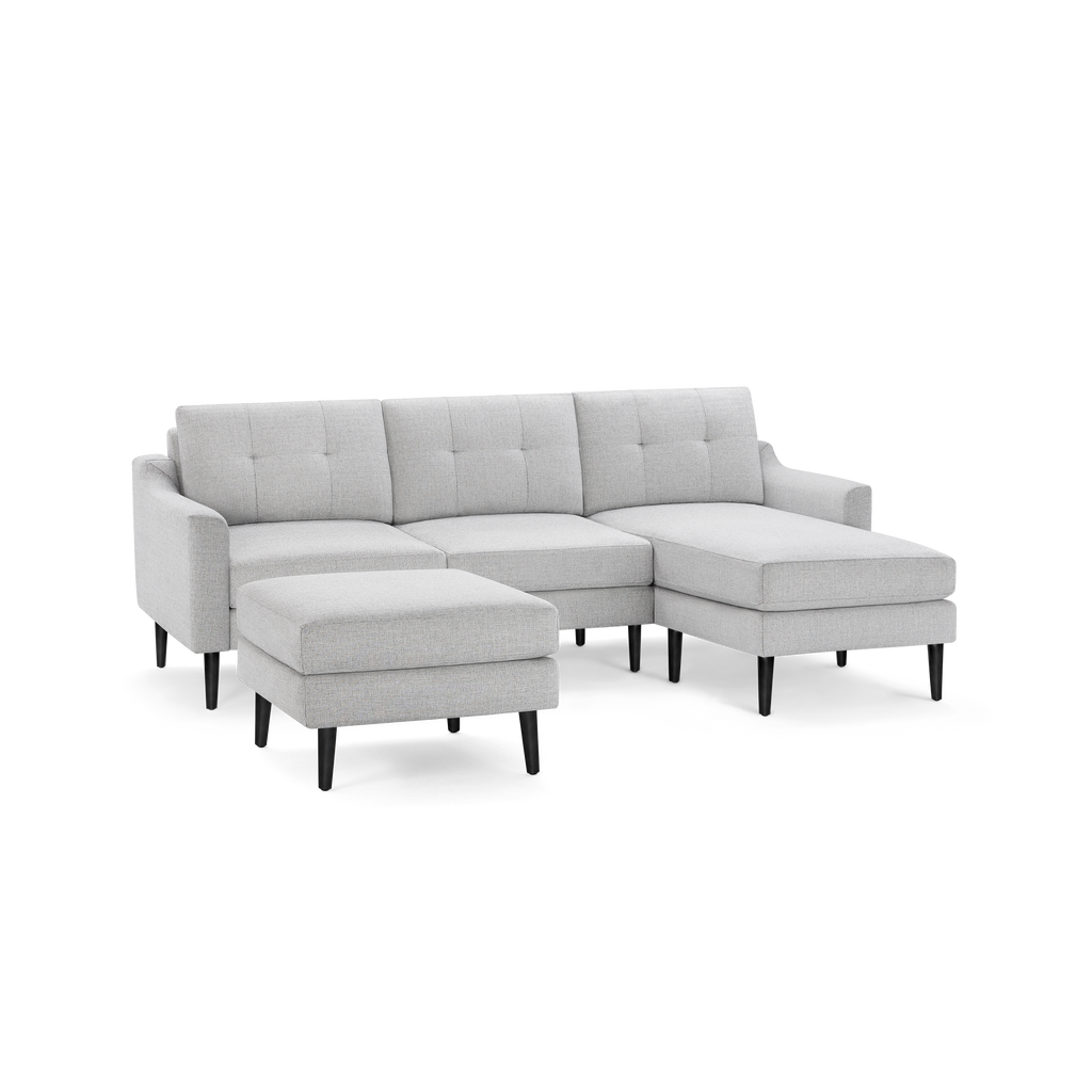 Light gray fabric sectional sofa with tufted back cushions, left armrest, chaise lounge on right, and matching ottoman, supported by black tapered legs.