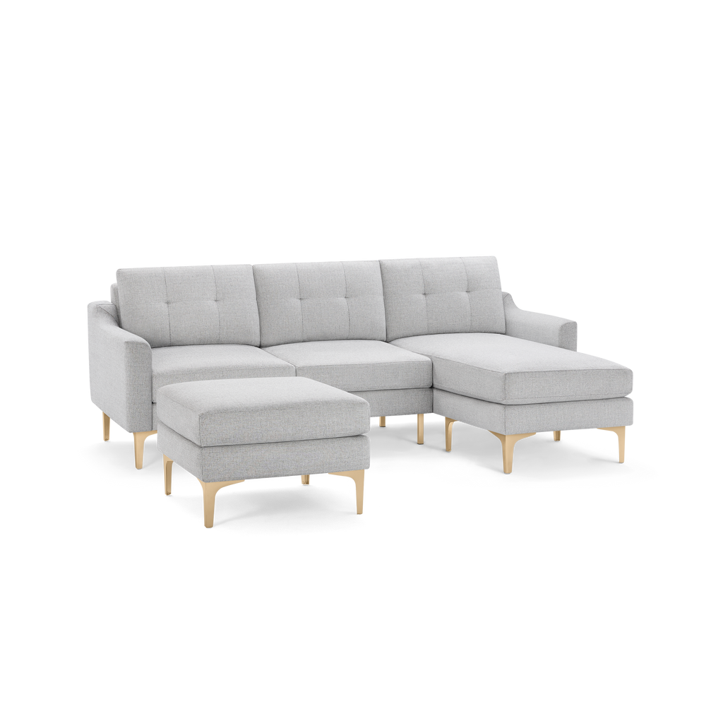 Light gray upholstered sectional sofa with tufted cushions, a chaise lounge on the right, and matching ottoman, both supported by gold metal legs.