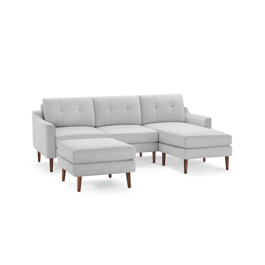 Light grey fabric sectional sofa with tufted back cushions, wooden legs, and a matching ottoman.
