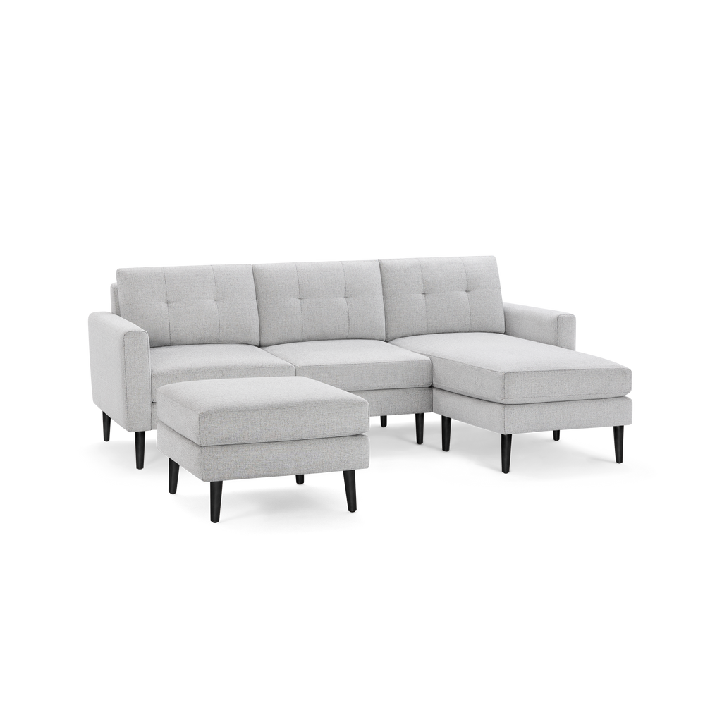 Light gray fabric sectional sofa with tufted back cushions, black tapered legs, and matching ottoman.