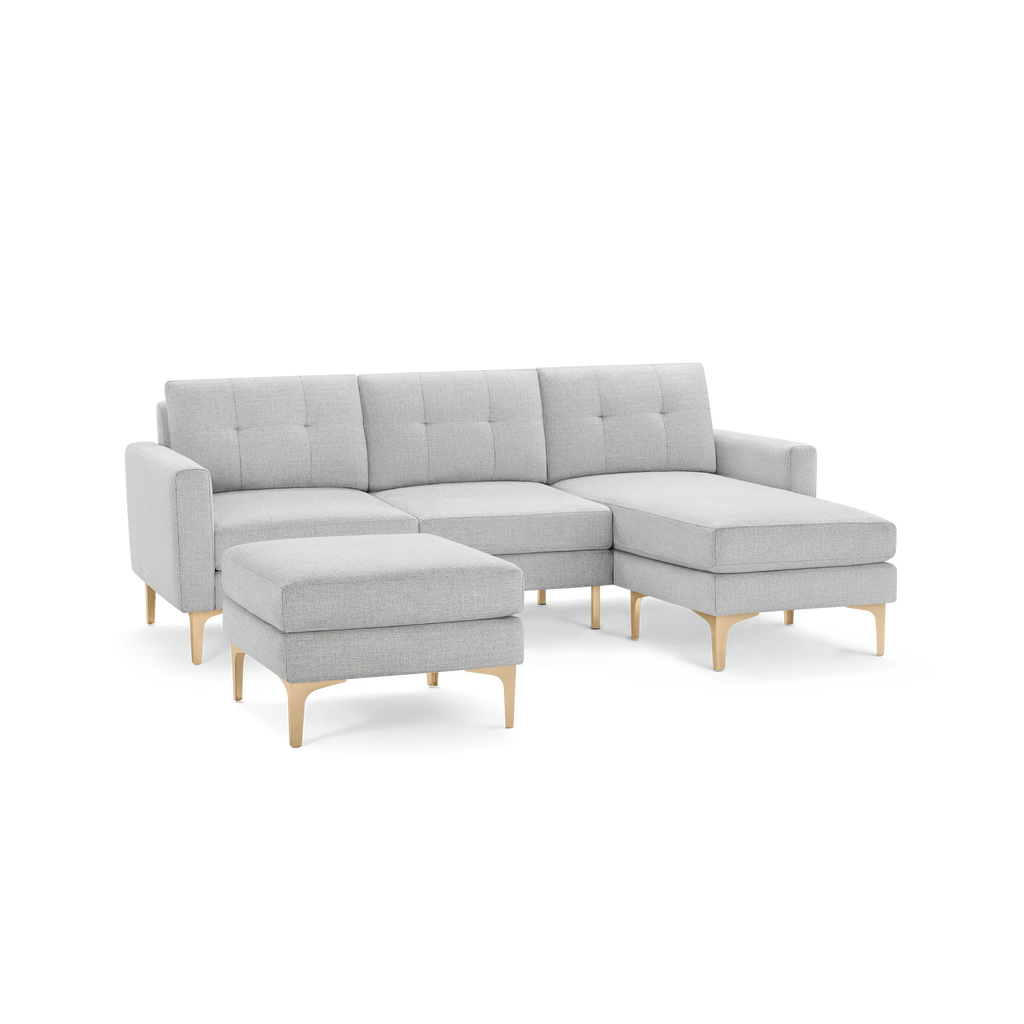 Light gray modern sectional sofa with tufted cushions and matching ottoman, supported by light wooden legs.