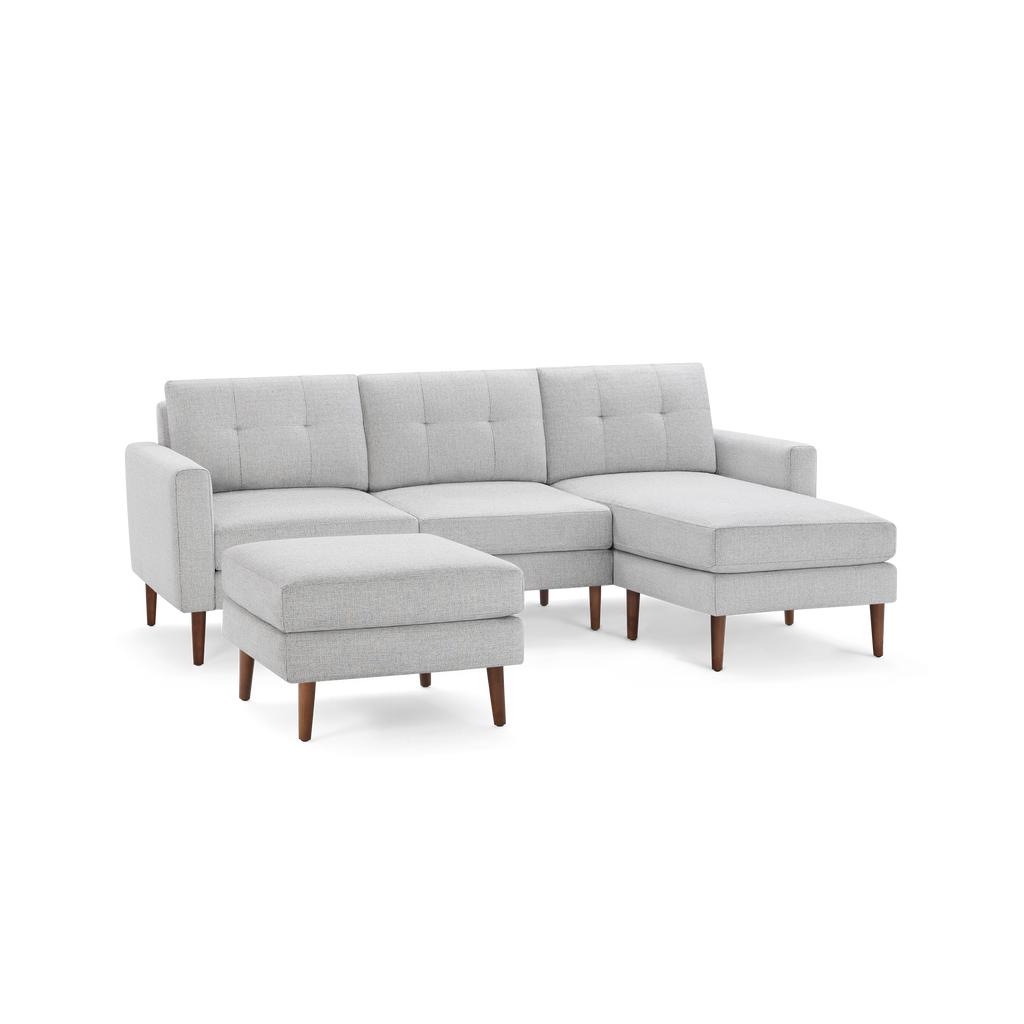 Light gray upholstered sectional sofa with tufted back cushions and wooden legs, including a matching ottoman.