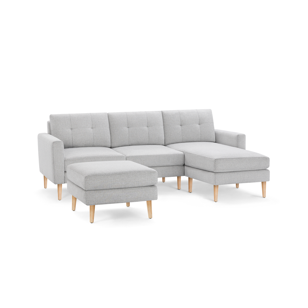 Light gray fabric L-shaped sectional sofa with tufted back cushions and light wood tapered legs, including a matching ottoman.