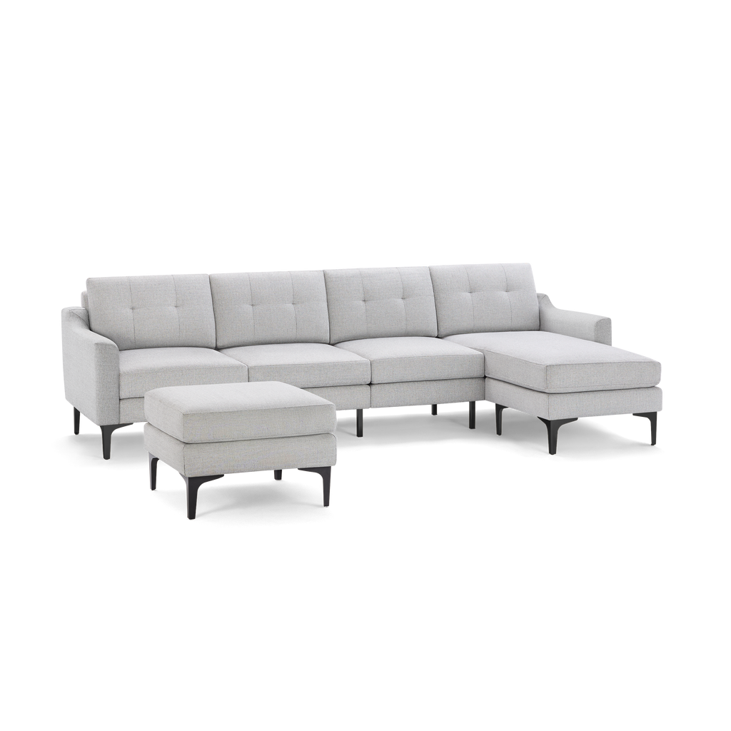Light gray sectional sofa with tufted cushions, chaise lounge on the right, and matching ottoman with black legs.