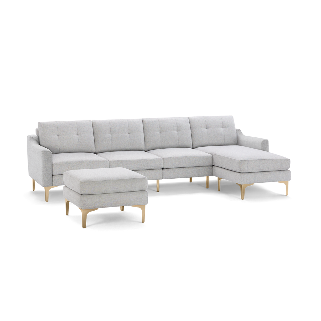 Light gray sectional sofa with tufted cushions, wooden legs, and a matching ottoman, modern and spacious design.