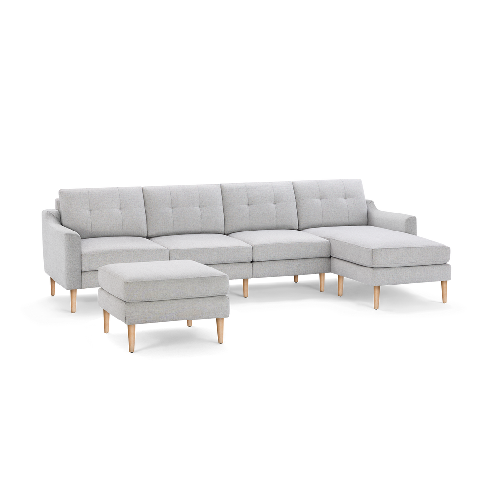 Light gray modern sectional sofa with tufted cushions, wooden legs, and a matching ottoman, on black background.
