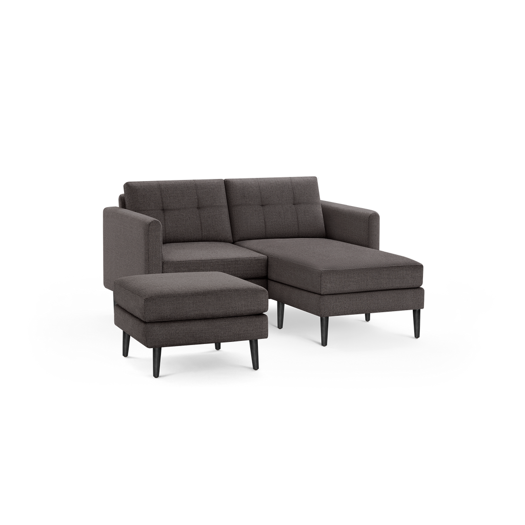 Dark gray fabric L-shaped sectional sofa with tufted backrest cushions and a matching ottoman, supported by black wooden legs.