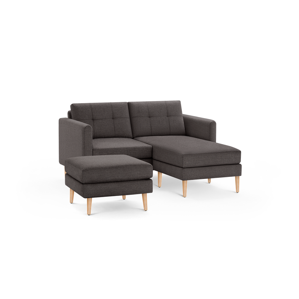 Dark gray fabric sectional sofa with tufted back cushions, wooden legs, and matching ottoman, modern and compact design.