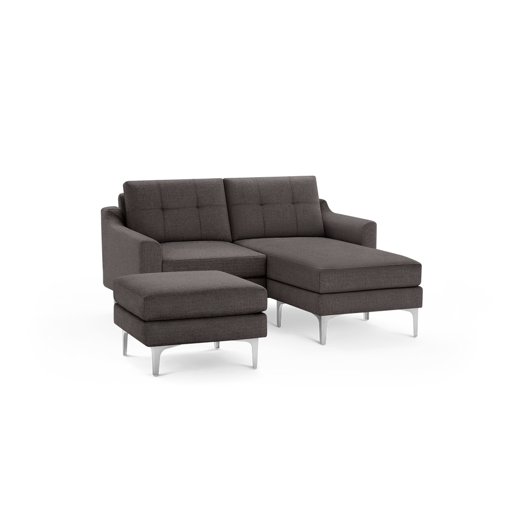 Modern dark gray fabric sectional sofa with chaise lounge and matching ottoman, featuring tufted cushions and silver metal legs.