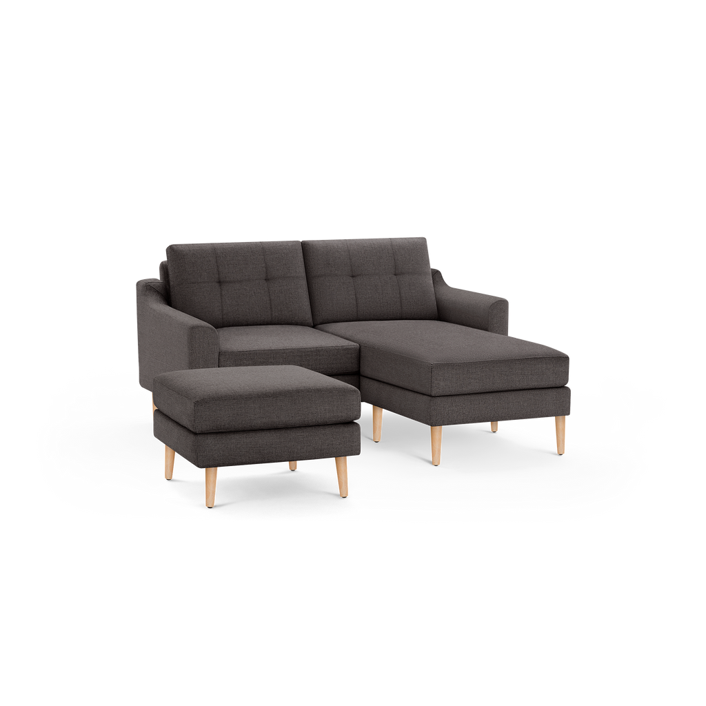 Dark gray fabric sectional sofa with tufted back cushions, angled armrests, wooden legs, and a matching ottoman.