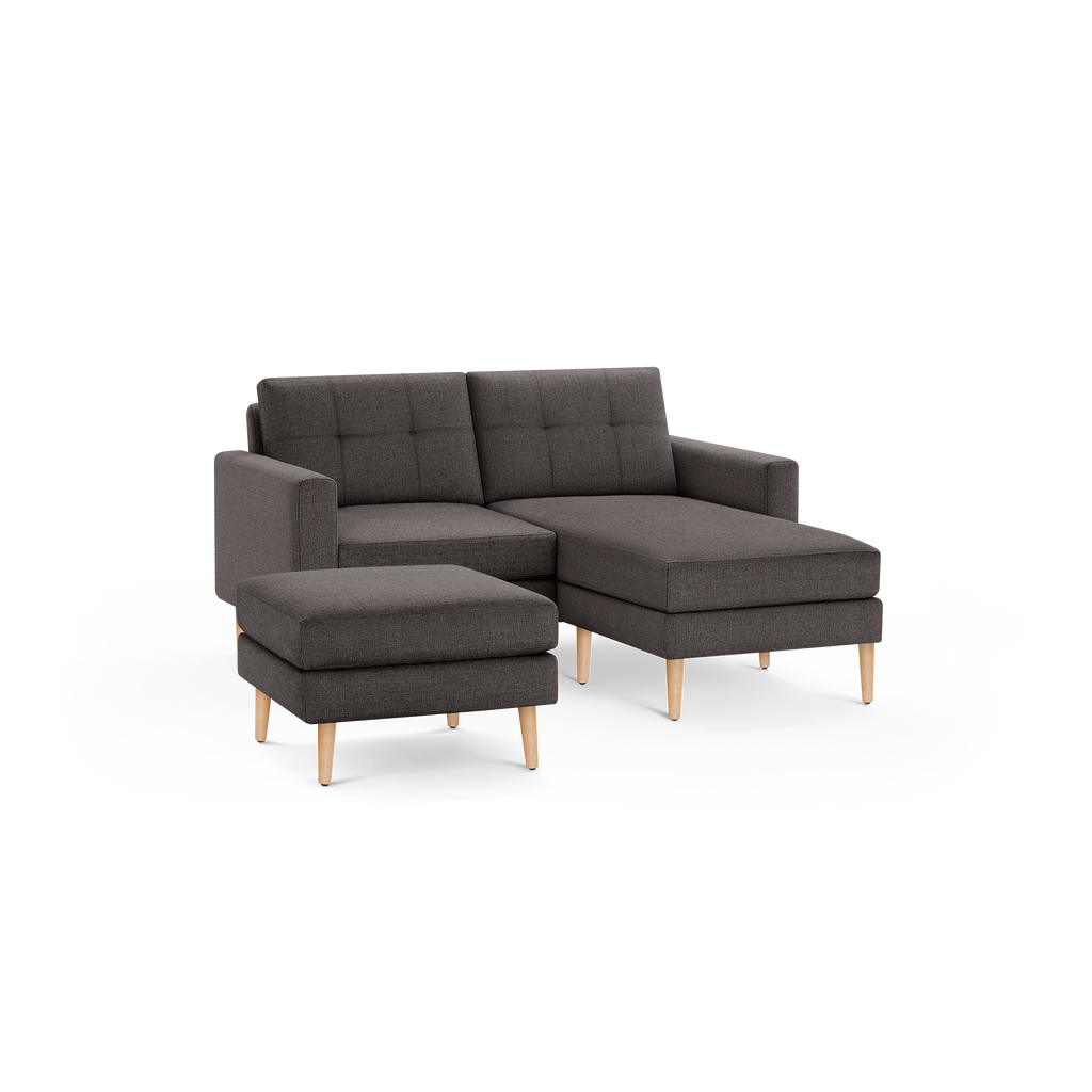 Dark gray fabric sectional sofa with tufted back cushions, wooden legs, and matching ottoman, displayed on a black background.
