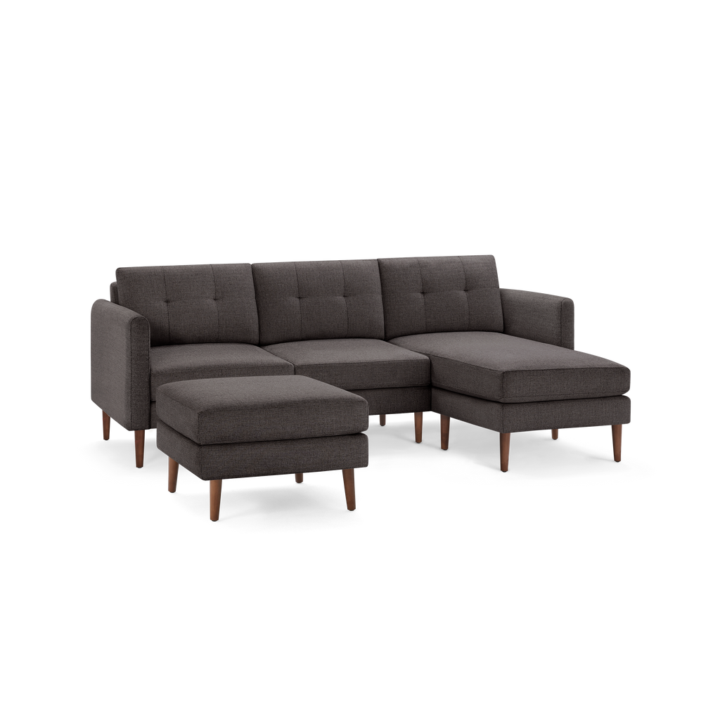 Dark gray fabric sectional sofa with tufted back cushions, wooden legs, and a matching ottoman, modern design.