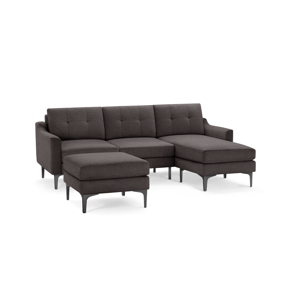 Dark gray modern sectional sofa with tufted cushions, metal legs, and a matching ottoman isolated on white background.