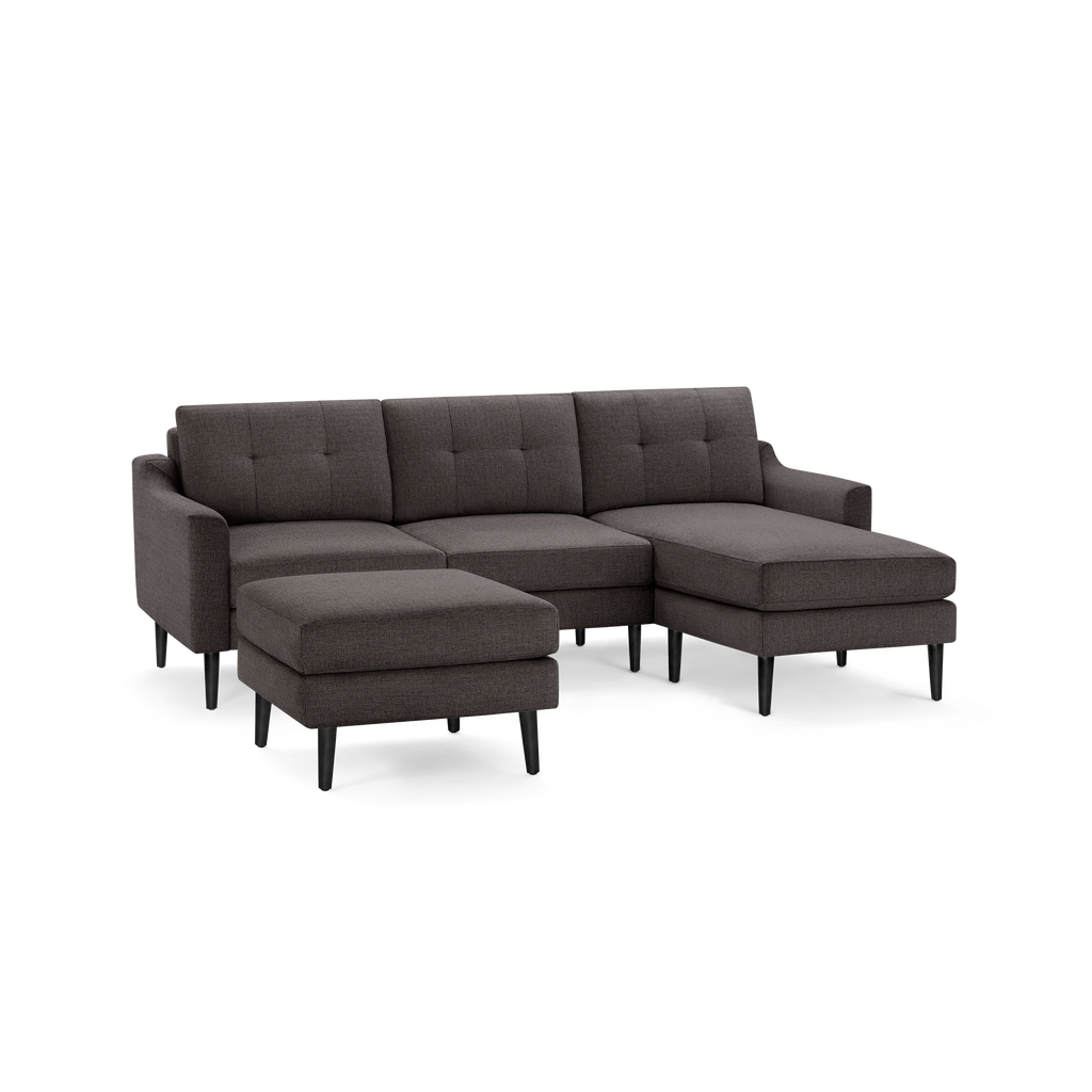 Dark gray sectional sofa with tufted back cushions, angled armrests, black tapered legs, and matching ottoman.