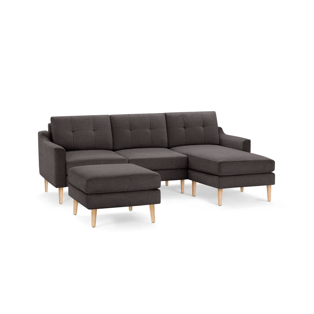 Dark gray fabric sectional sofa with tufted cushions, wooden legs, and a matching ottoman.