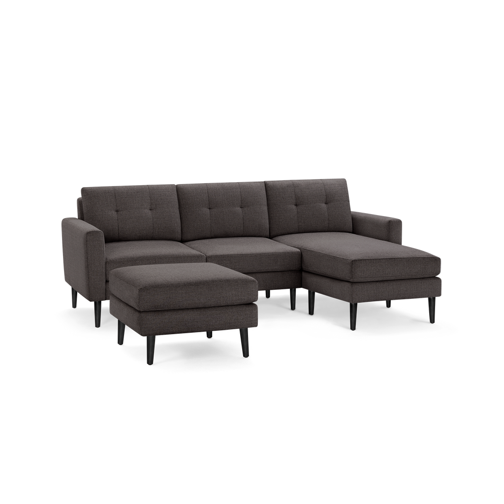 Dark gray fabric sectional sofa with tufted back, chaise lounge on the right, and matching ottoman on black legs.