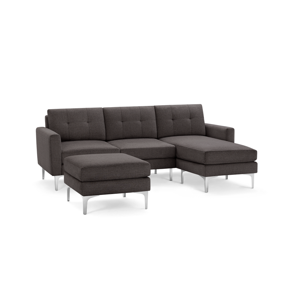 Modern dark gray fabric sectional sofa with chaise lounge and matching ottoman, featuring tufted back cushions and metal legs.