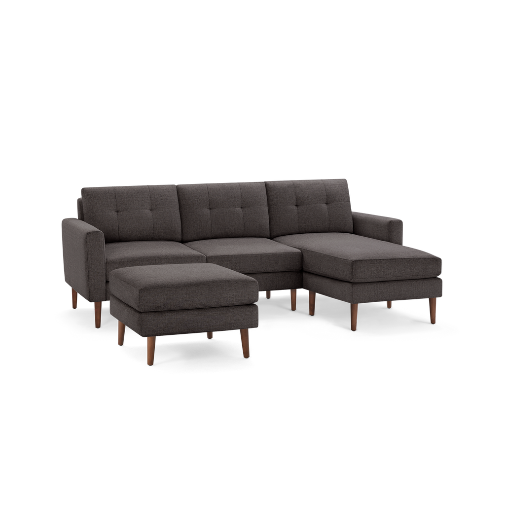 Dark gray upholstered sectional sofa with tufted cushions, wooden legs, and matching ottoman, modern design.