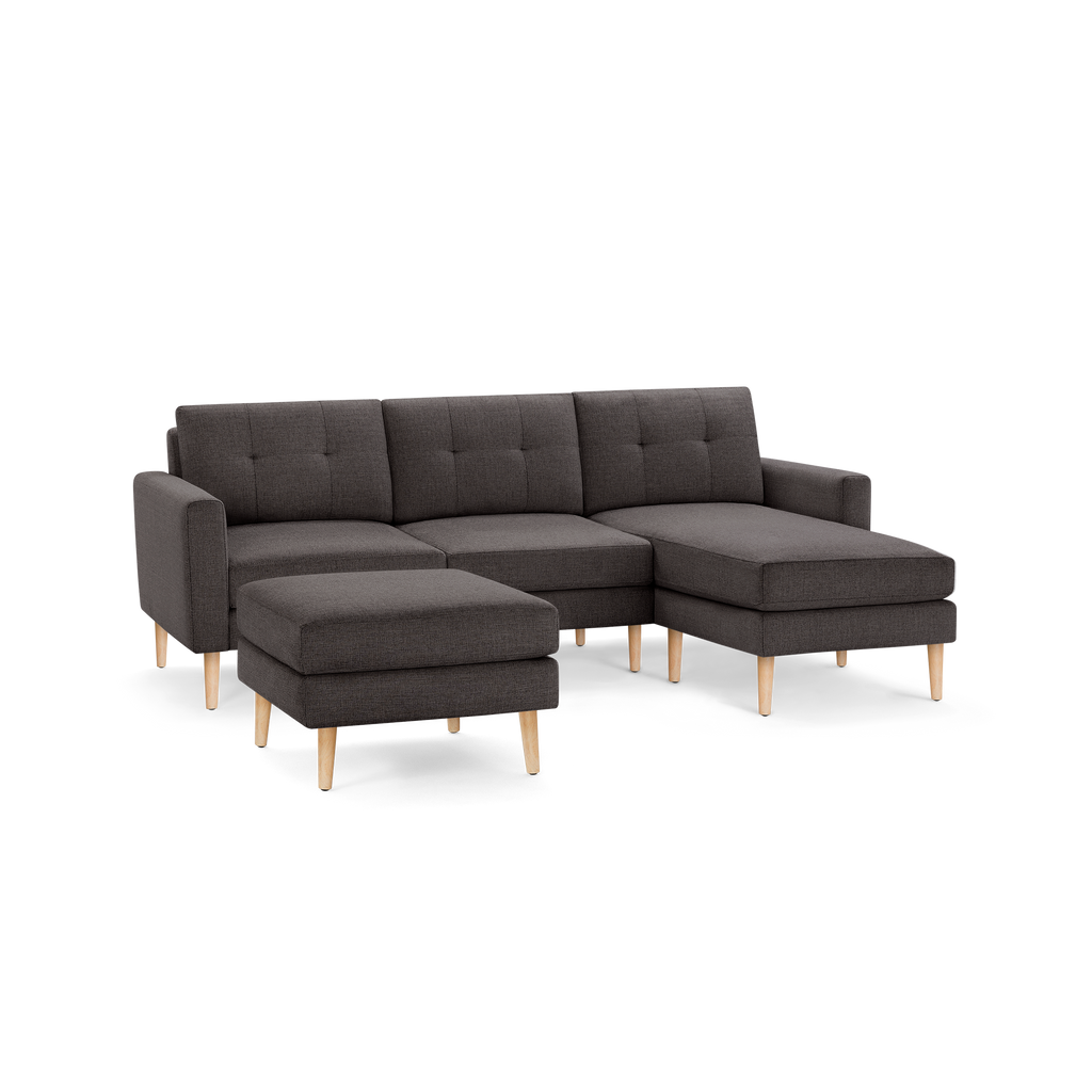 Modern dark gray fabric sectional sofa with tufted cushions, wooden legs, and matching ottoman on a black background.