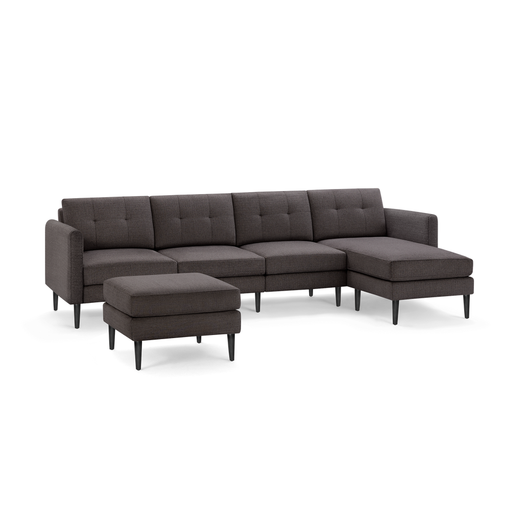 Dark gray fabric sectional sofa with chaise lounge on the right and a matching ottoman, featuring tufted cushions and black tapered legs.