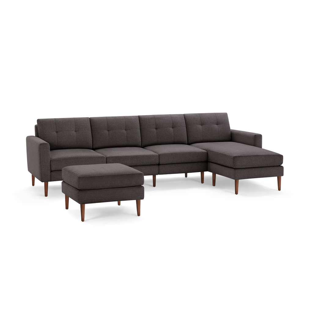 Dark gray fabric sectional sofa with tufted cushions, wooden legs, and matching ottoman on a black background.