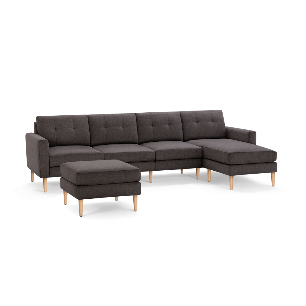 Dark gray fabric sectional sofa with wooden legs and matching ottoman, featuring tufted back cushions and a chaise lounge on the right side.